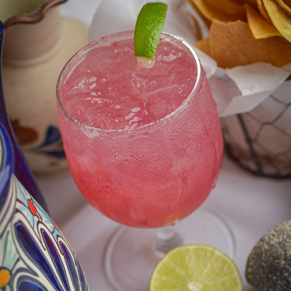A vibrant pink La Olla Mexican Cafe margarita with a lime wedge, surrounded by chips and pottery.